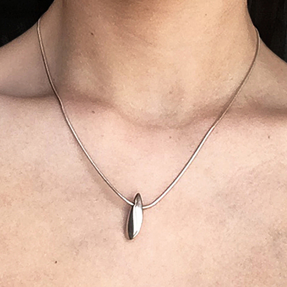 The plain side shell pendant has a smooth organic form. It is approx 22mm long with a width of 4mm and a depth of 8mm at the widest point. The pendant comes on a silver snake chain.