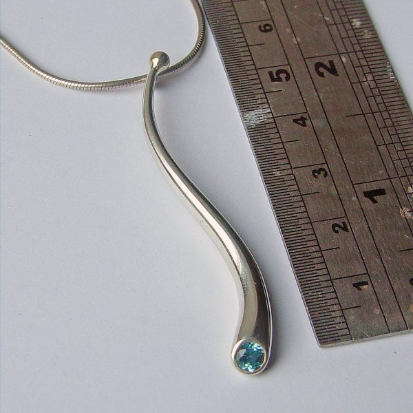 An elegant long curving wiggly pendant with 4mm faceted blue topaz and 18ct gold bead on a silver snake chain. The solid silver wiggly pendant tapers from 5mm and is approx 50mm long. The sweeping curves enhance the beautiful pure design.