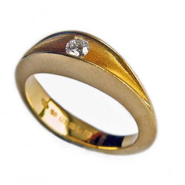The 18ct yellow gold diamond shell ring is an elegant and unusual sculptural ring. The 10pt diamond is set to allow maximum light around the stone. The ring has a lovely smooth organic shape. The comfortable solid band is split across the top to reveal a sparkling 0.1ct diamond trapped within the gold interior. An unusual statement ring which is also makes the perfect engagement ring. Brilliant 0.1ct vsfg diamond tension set in satin finished 18ct yellow gold. Dimensions are 5mm wide & 5mm depth.